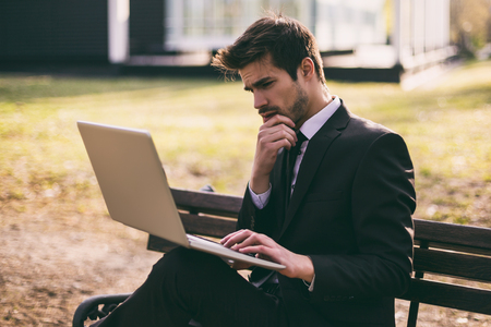 Worried businessman using laptop while sitting outdoor.Toned image.の写真素材
