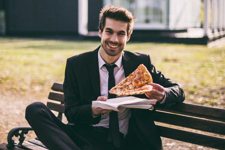 Elegant businessman enjoys eating pizza on his lunch break while sitting outdoor.Toned image.の写真素材