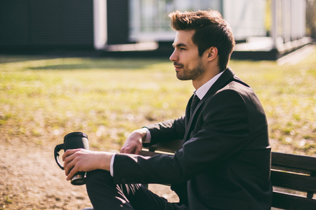 Elegant businessman enjoys drinking coffee while sitting outdoor.Toned image.の写真素材