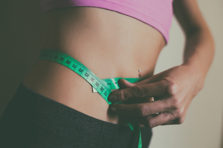 Fit woman measuring her tin waist  with a tape measure.の写真素材