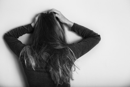 Depressed woman standing alone in front of wall.Intentionally black and white image.の写真素材