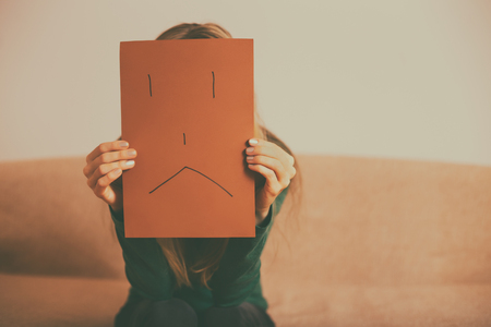 Depressed woman sitting alone at sofa and holding paper with sad face.Toned image.の写真素材