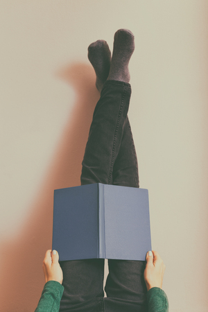 Woman resting and reading book with legs up in front of the wall.Toned photo.の写真素材