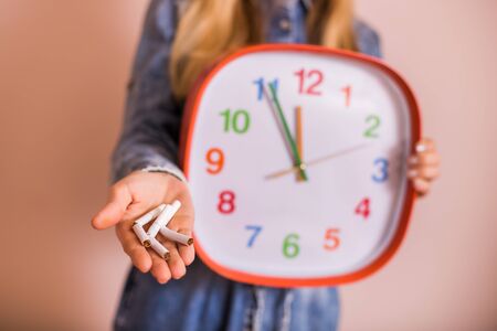 Woman holding broken cigarettes and clock in front of the wall.Quitting smoking concept.の写真素材