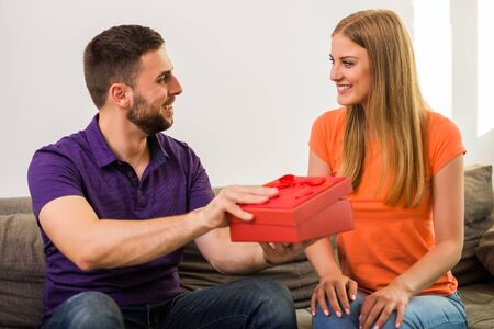 Man giving present to his wife while they sitting on sofa at their home.の写真素材