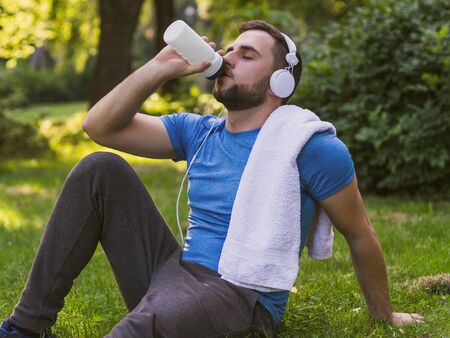 Handsome man with headphones  drinking water and resting after exercise in the park.の写真素材
