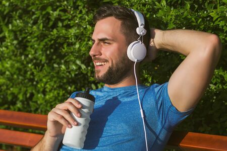 Handsome man with headphones  drinking water and resting after exercise in the park.の写真素材