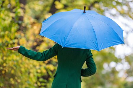 Woman holding blue umbrella and checking for rain while standing in the park.の写真素材