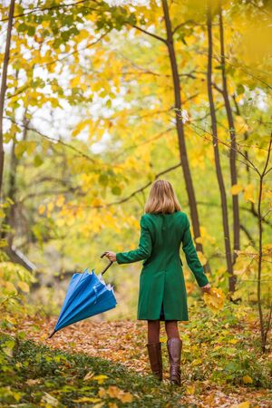 Woman holding umbrella and fall leafs while walking in the park.の写真素材