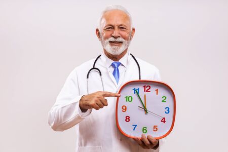 Portrait of senior doctor holding clock on gray background.の写真素材