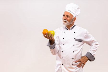 Image of senior chef holding  fruit and thinking on gray background.の写真素材