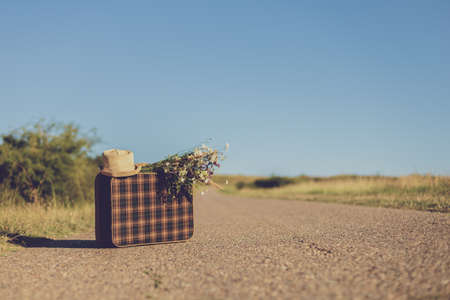 Image of  old suitcase,hat and flowers on the country road.の写真素材