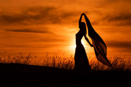 Happy woman dancing and holding scarf while enjoys spending time at sunset.の写真素材