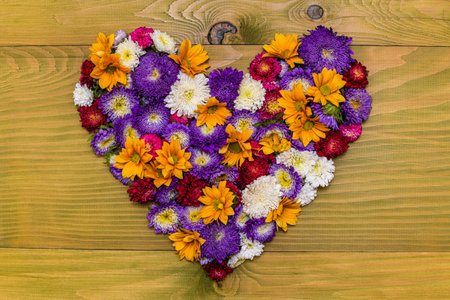 Image of heart shape made of  beautiful flowers on wooden background.