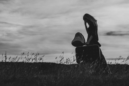 Image of  sad woman holding suitcase and heart shaped balloon. Black and white photo.