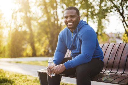Man resting on bench after exercise and drinking water .