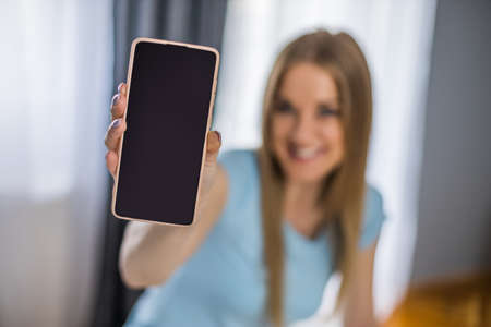 Young woman holding mobile phone with blank screen for your advert. Focus on phone.の写真素材
