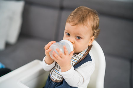 Cute baby boy  drinking water while sitting in a high chair.の写真素材