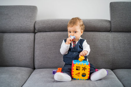 Cute little baby boy playing with toys while sitting on sofa.