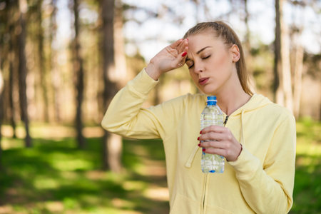 Tired woman  drinking water after exercise  in the nature.