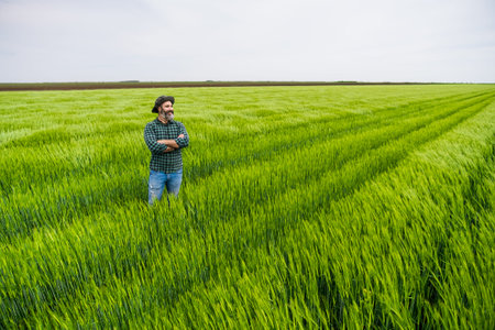 Happy farmer is standing in his growing wheat field.