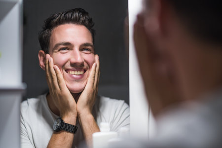 Man is applying aftershave while looking himself in the mirror.の写真素材