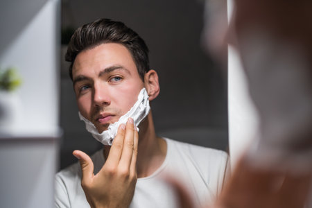Man applying shaving cream while looking himself in the mirror.の写真素材
