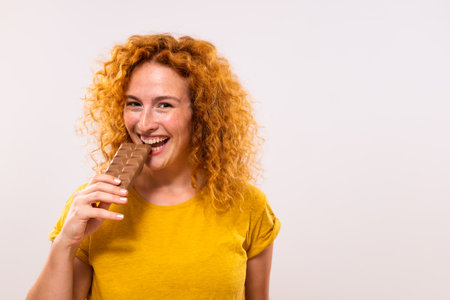 Portrait of happy cute ginger woman enjoys eating chocolate.の写真素材