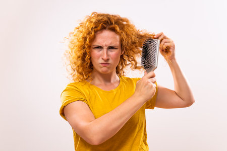 Angry ginger woman holding hairbrush and combing her curly  hair.の写真素材