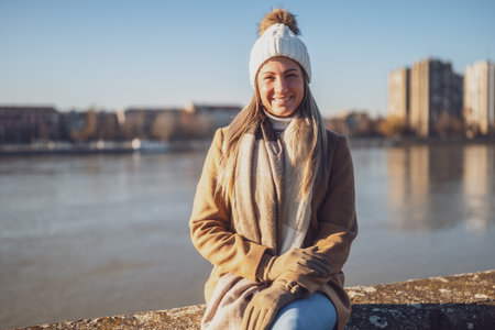 Beautiful woman in warm clothing enjoys resting by the river on a sunny winter day.  Toned image.の写真素材