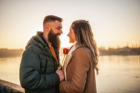 Happy man giving red rose to his woman while they enjoy spending time together on a sunset.の写真素材