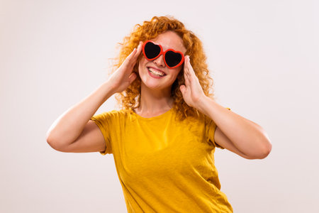 Image of happy ginger woman with red heart shaped sunglasses.の写真素材