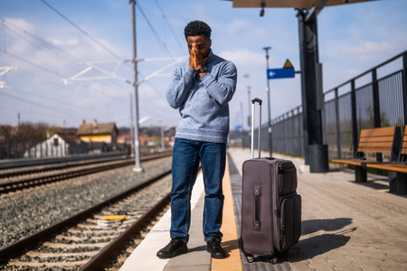 Worried man with a suitcase standing on a railway station.の写真素材