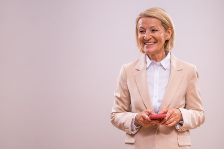 Portrait of successful mature businesswoman using phone on gray background.の写真素材
