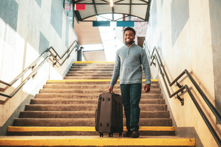 Happy man with suitcase walking down a stairs in railway station.の写真素材