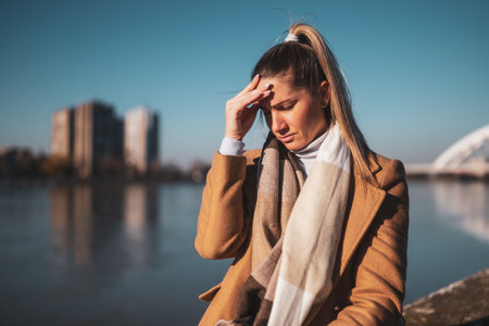 Worried woman having headache while sitting by the river. Toned image.の写真素材