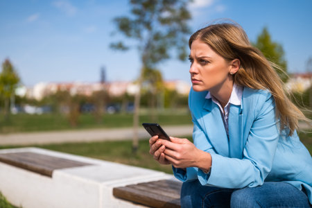 Angry businesswoman using mobile phone while sitting on the bench outdoor.の写真素材