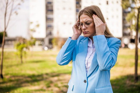 Worried businesswoman with eyeglasses is having a headache while standing outdoor.の写真素材