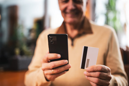 Close up photo of senior man using mobile phone and credit card while sitting in cafe. Focus on...