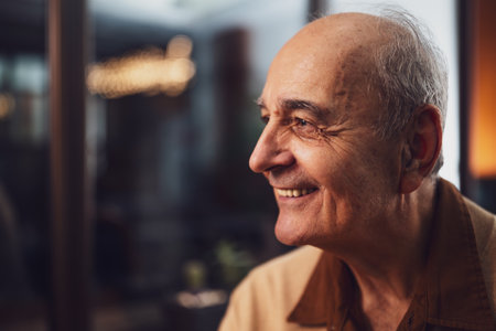 Close up portrait of smiling senior smiling and looking away while sitting in the cafe at evening.の写真素材
