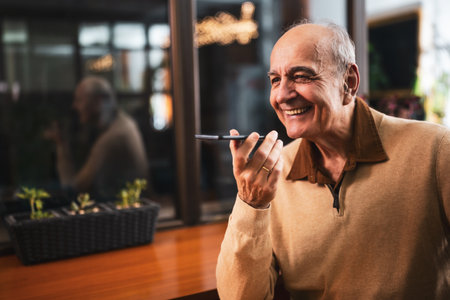 Smiling senior man talking on the smart phone and drinking coffee while sitting in cozy city bar.の写真素材