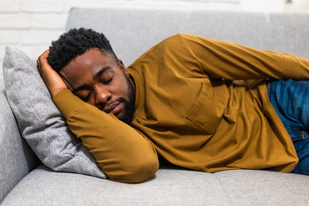 Tired African American man enjoying sleeping on sofa at his cozy home.の写真素材