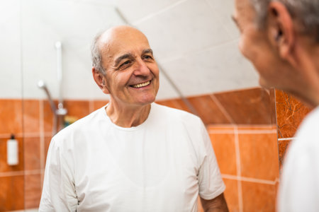 Portrait of happy senior man with gray hair looking into the bathroom mirror and enjoying his daily self-care routine.の写真素材
