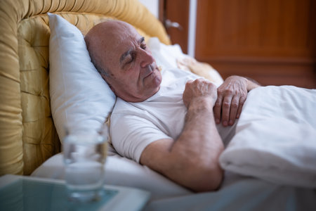 Senior man calmly sleeping in bed with glass of water next to him on night table in his bedroom.の写真素材
