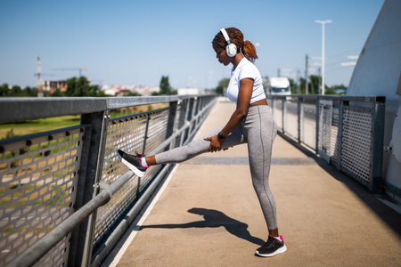 Young African-American woman in sport clothing exercising and stretching while listening to music...