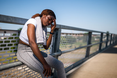 Sporty African woman shows signs of sadness and disappointment while resting after running outdoor.の写真素材