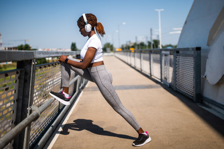 A young adult African American woman in sportswear performing leg stretches as part of her warm-up for physical activity.の写真素材