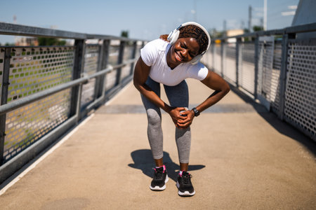 Worried young African-American woman in sportswear having sport injury during exercising outdoor. She is having pain in her knee.の写真素材