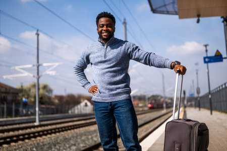 Portrait of happy African -American man with suitcase standing on railway station.の写真素材