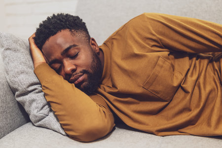 Tired young African man peacefully sleeping on sofa at his cozy home.